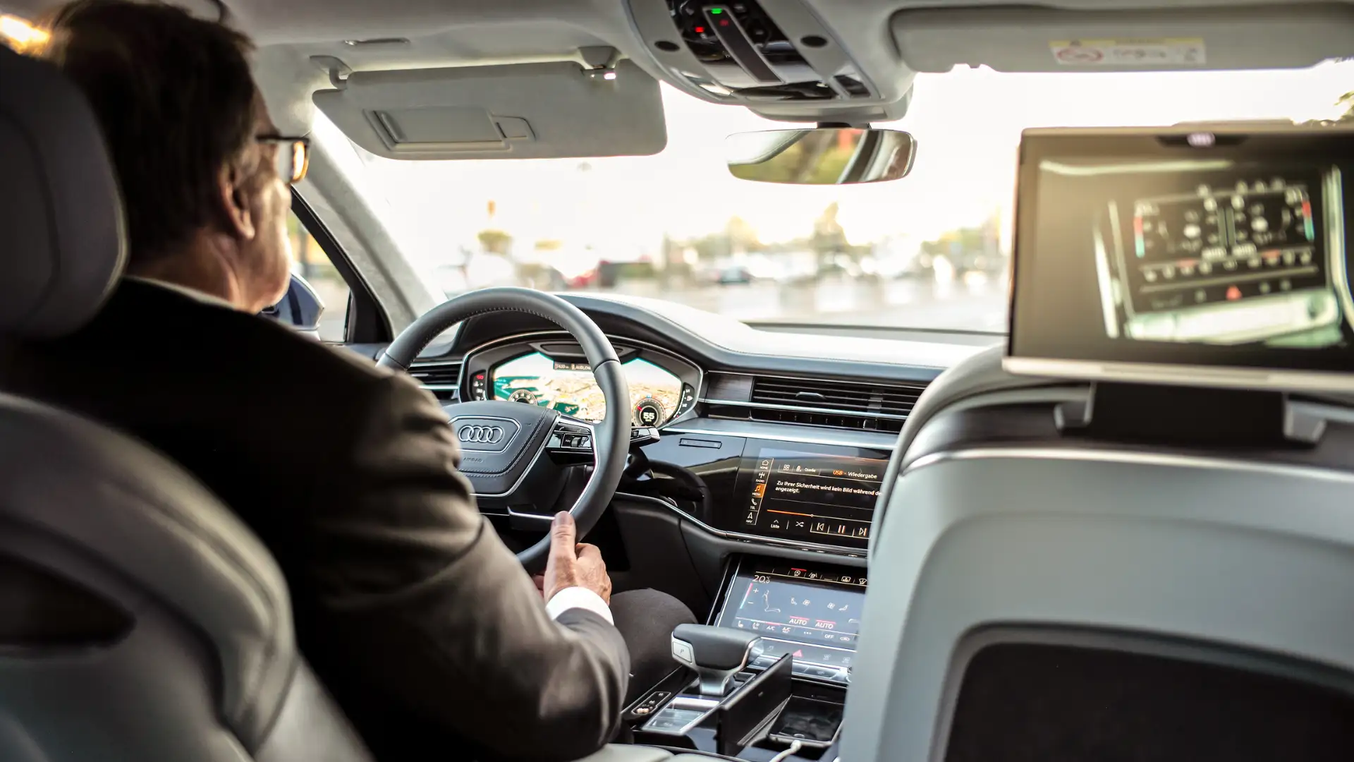 Interior view of a car showing the driver’s hands on the steering wheel, with a focus on the modern dashboard and controls