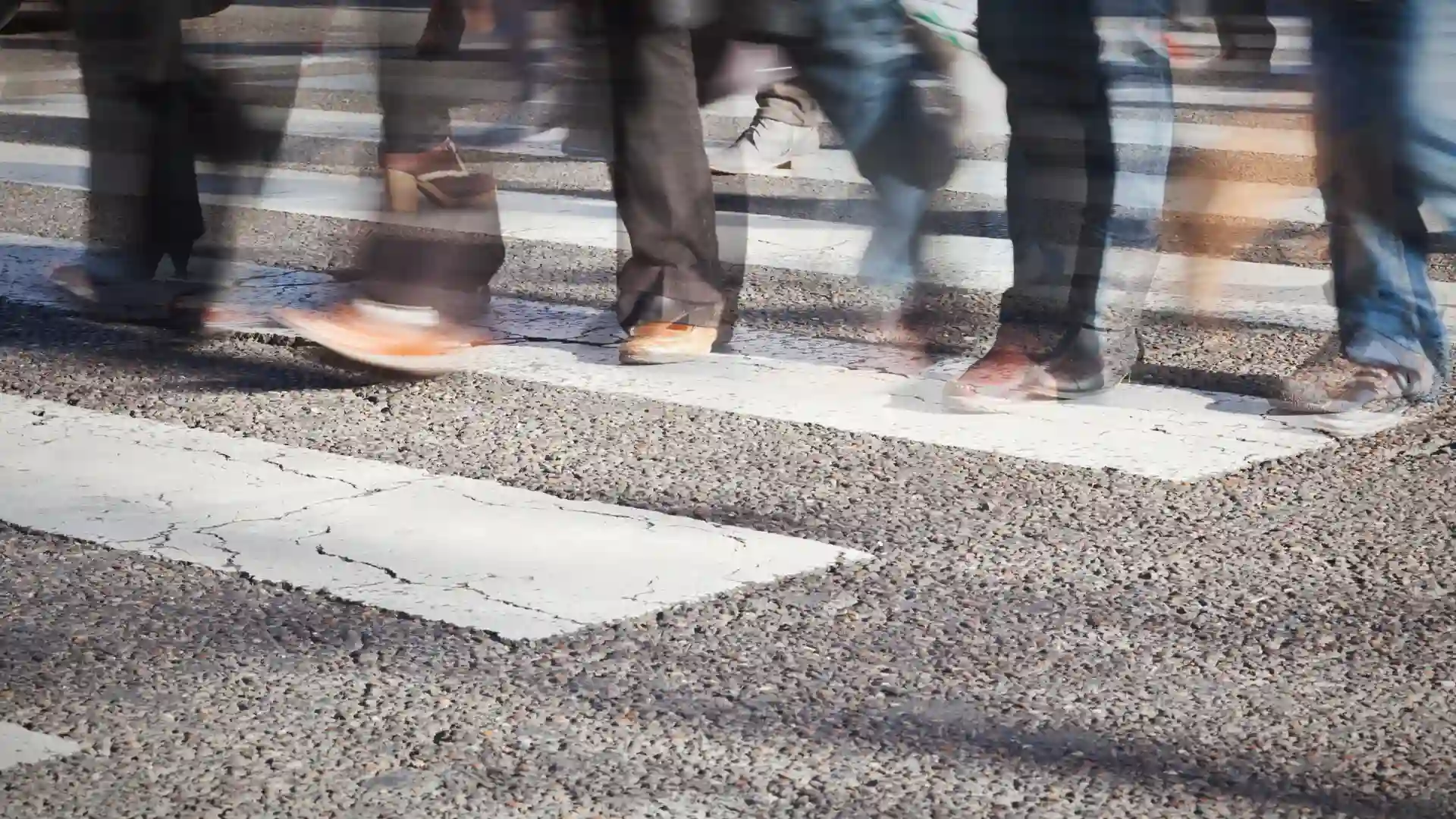 Blurry motion of people walking across a crosswalk, with an emphasis on feet and legs.