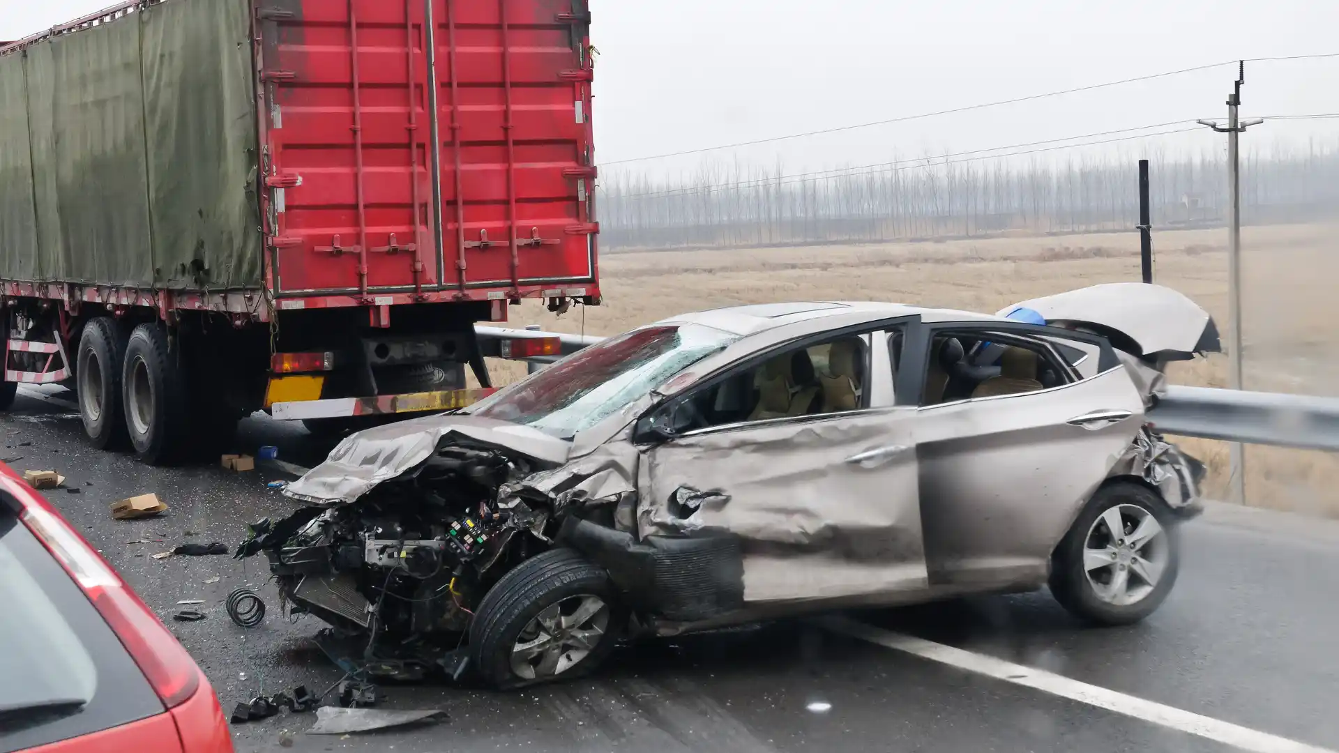 A severe car crash on the road involving a small vehicle and a large truck, with visible damage to the front of the car.