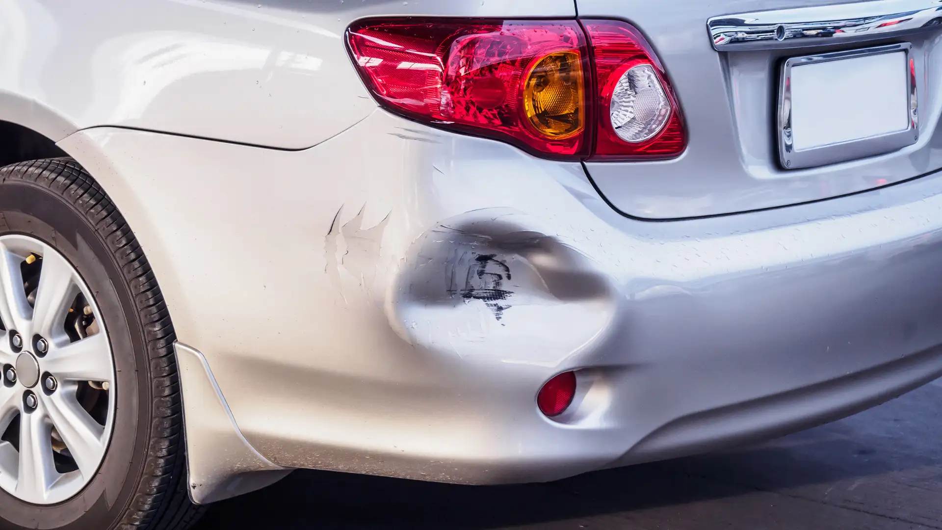 Close-up of a white car with a dent on the rear bumper