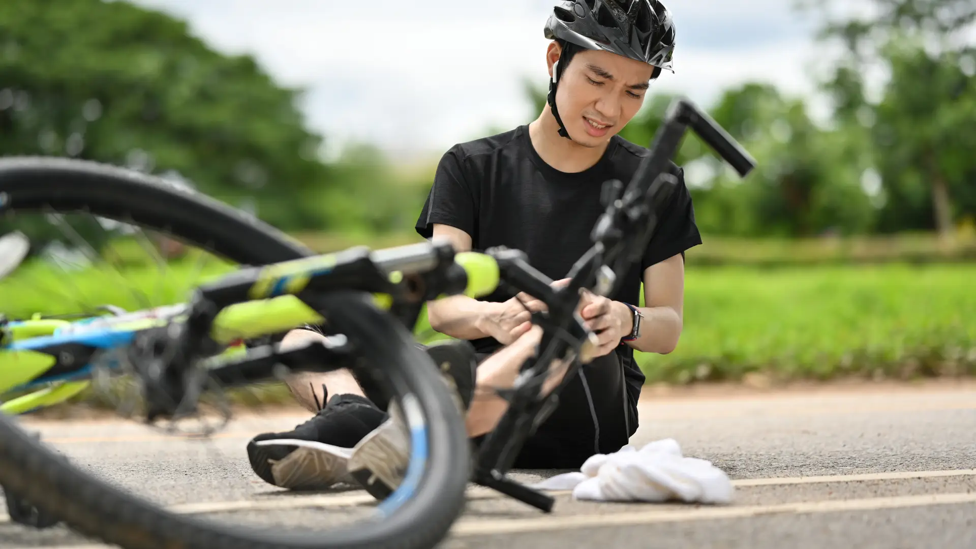 Injured cyclist sitting on the road holding his arm next to a fallen bicycle, wearing a helmet