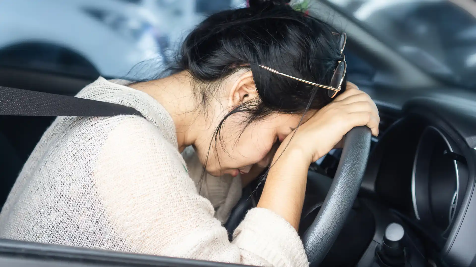 Distressed woman leaning on a steering wheel inside a car, appearing emotionally overwhelmed after an incident.