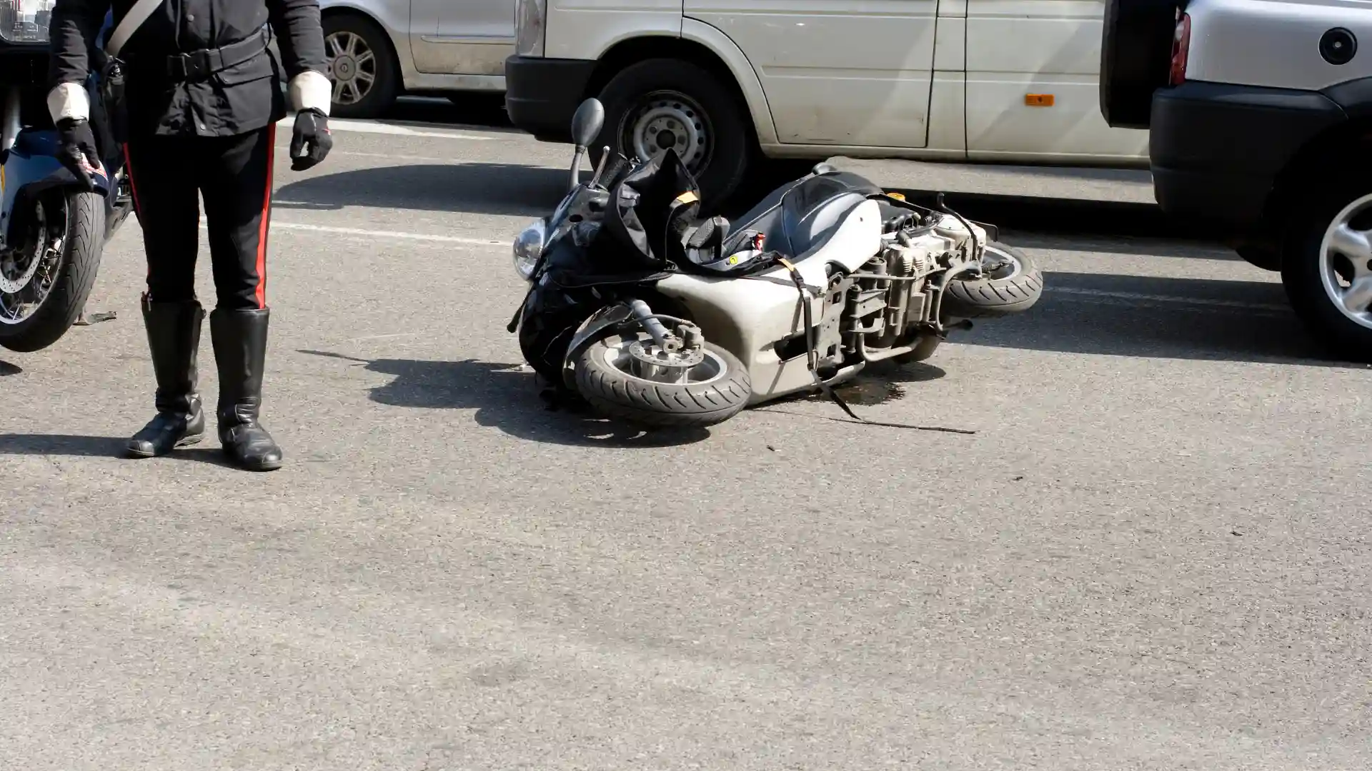 Motorcycle lying on its side on the road after an accident, with cars parked nearby.