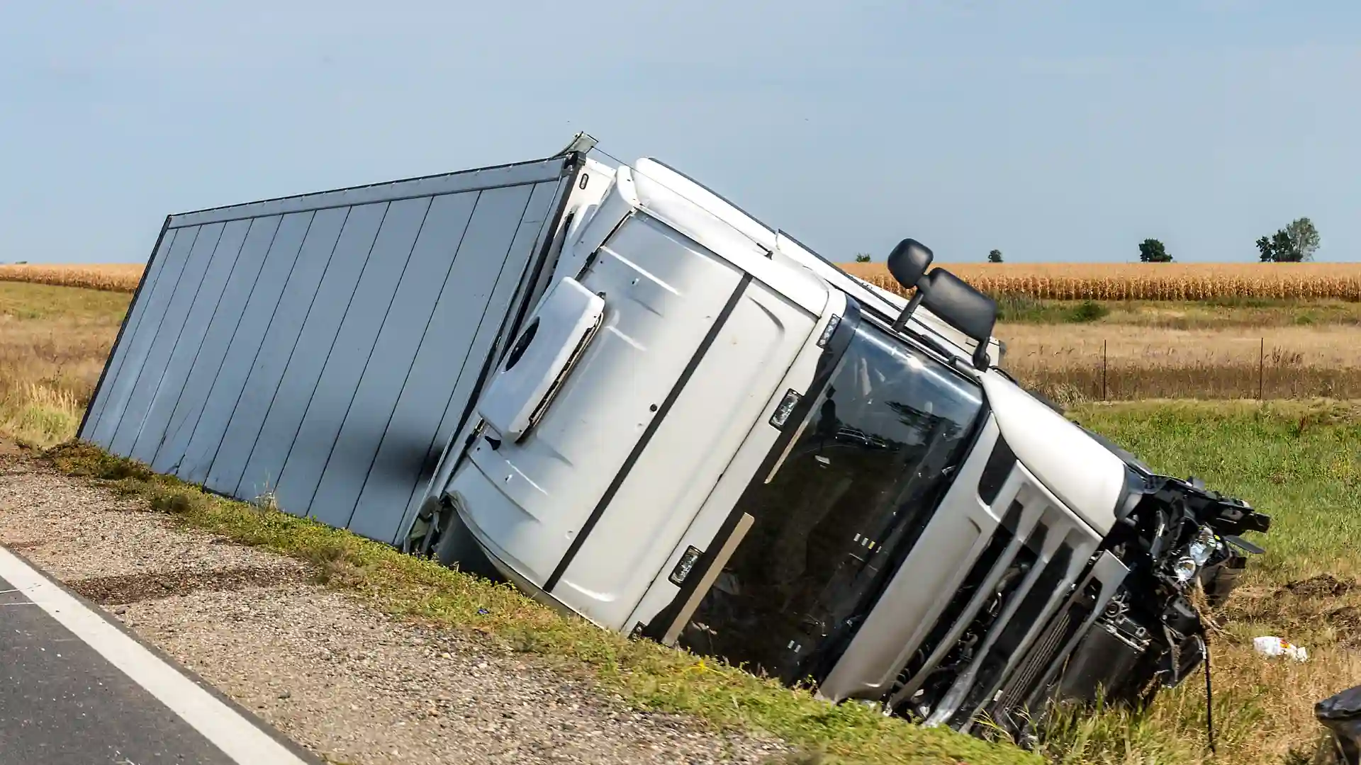 Large white semi-truck overturned on the side of a rural road
