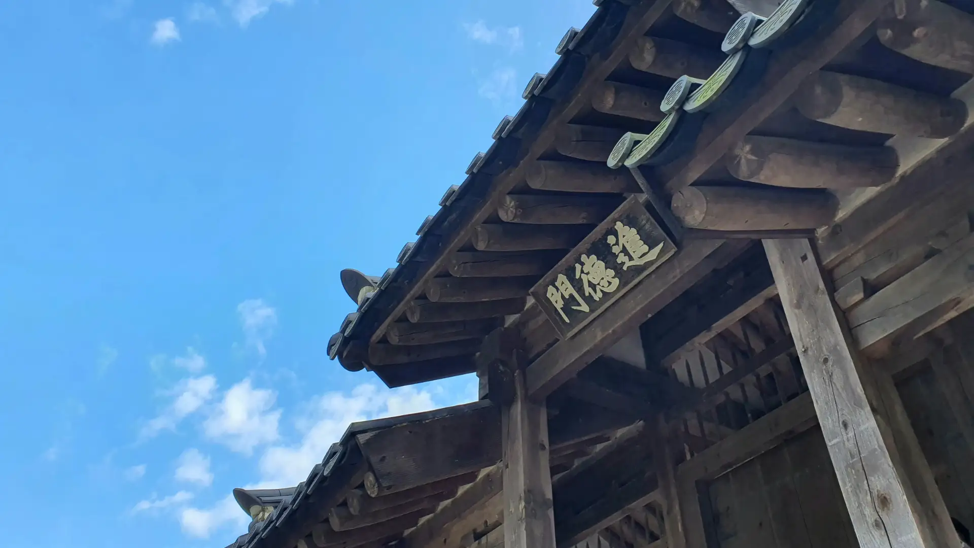 Traditional wooden roof structure with Chinese characters under a blue sky.