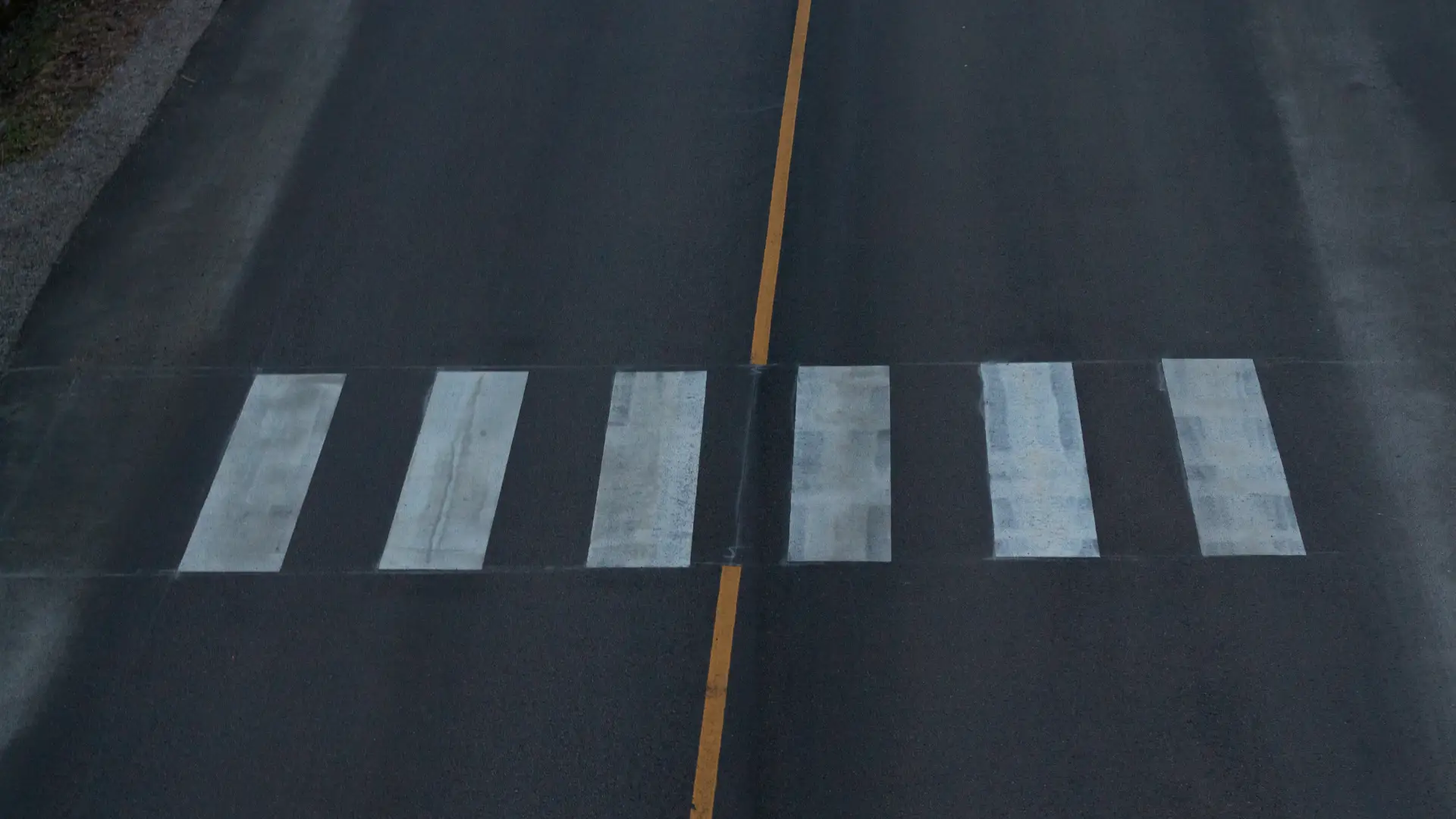 An aerial view of a pedestrian crosswalk on an empty road, with clear white lines.