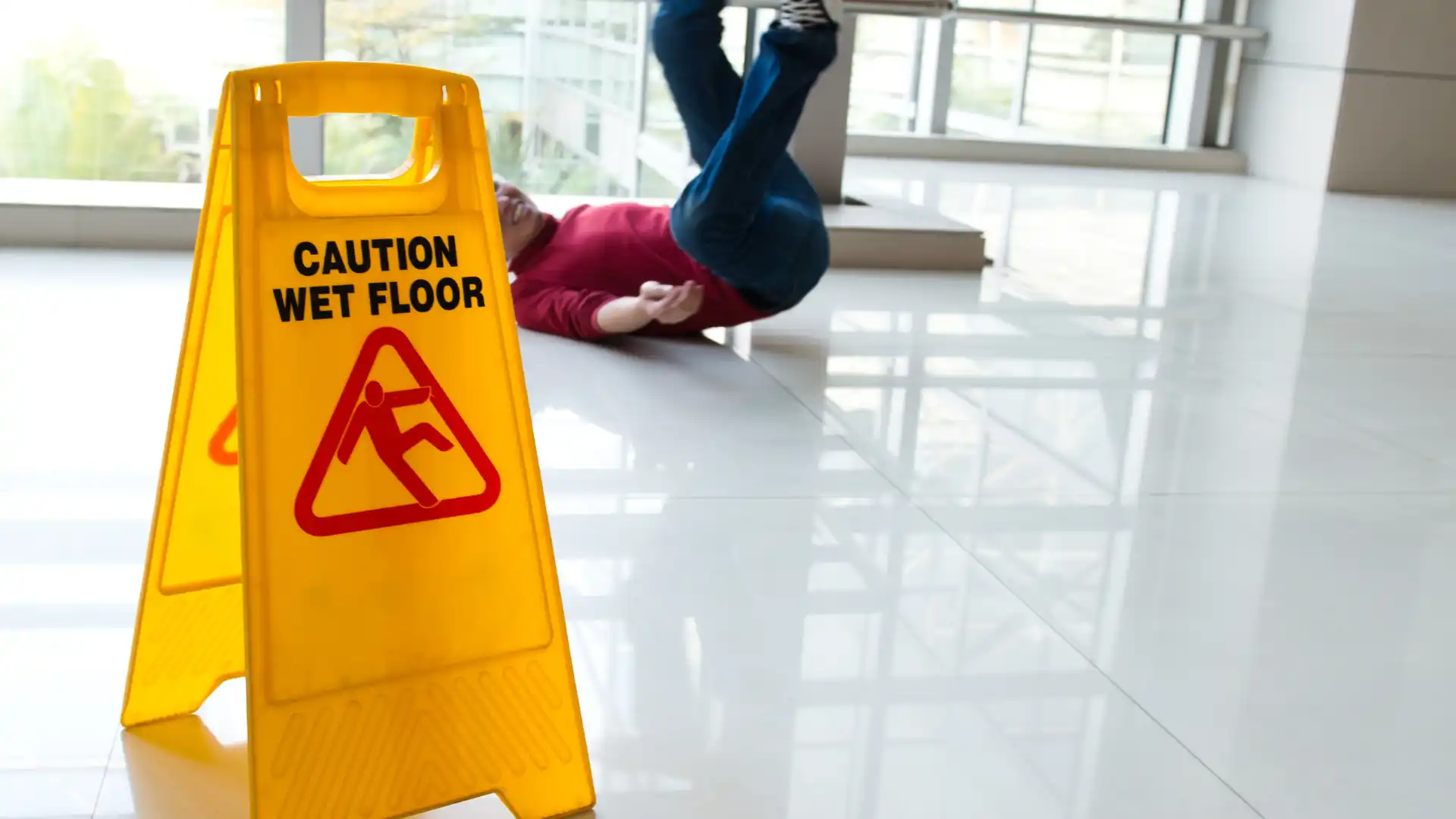 Person slipping on wet floor near caution sign.