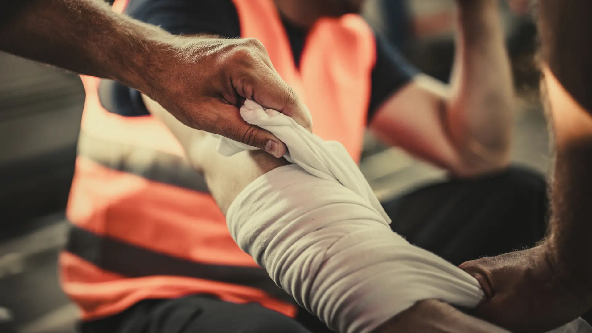Person wrapping a bandage around an injured arm at a work site.